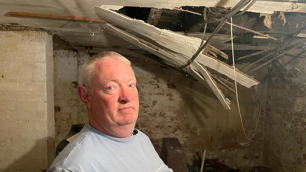 Man stands in cellar with crumbling roof and electrics hanging down