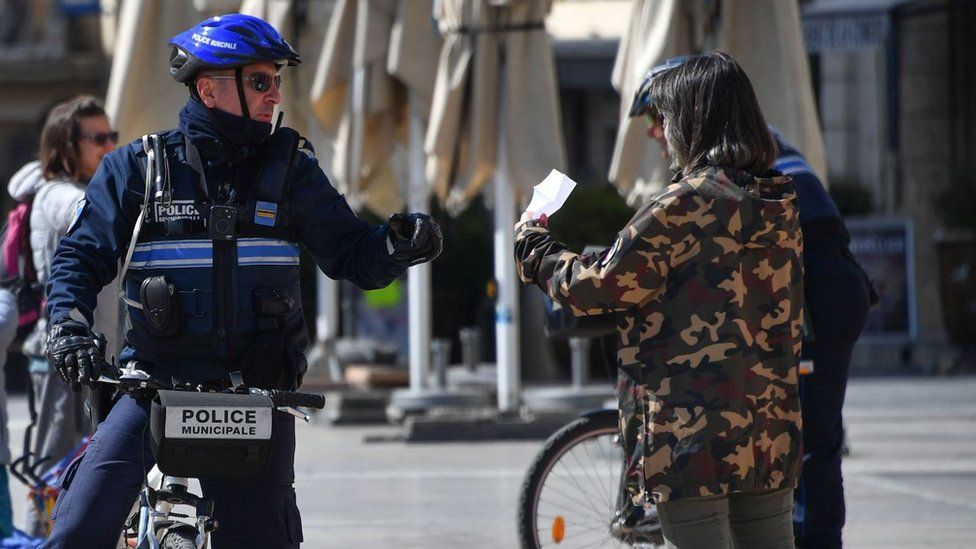 A municipal police officer controls a passer-by for her certificate as they monitor people's movement in Montpellier, 25 March 2020