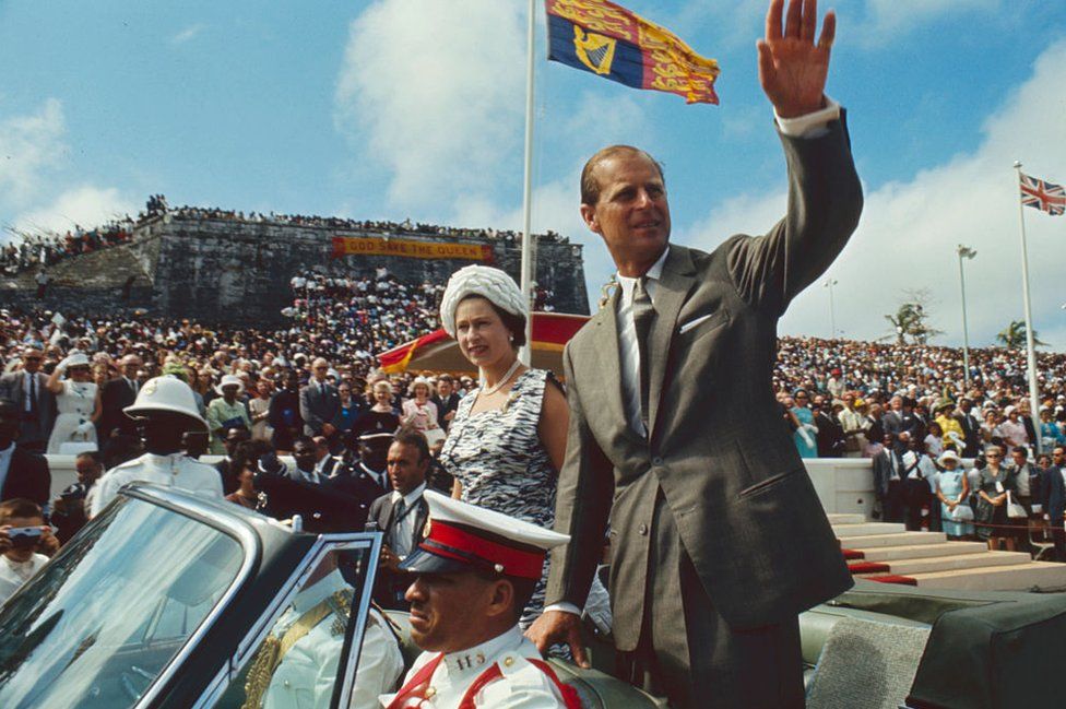 During a royal visit, British monarch Queen Elizabeth II and her husband, Prince Philip, Duke of Edinburgh, wave from an open-top convertible to onlookers at Clifford Park, Nassau, Bahamas, 28 February 1966.