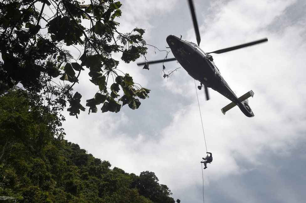 A Thai Airforce worker drops in by helicopter into a clearing in the forest near a possible overground opening to the Tham Luang cave
