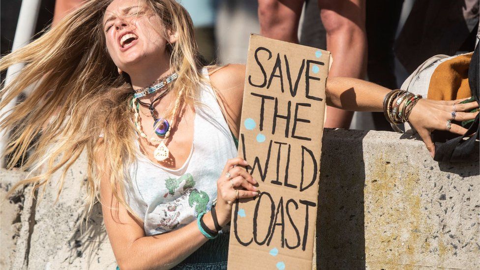 A woman holding a placard which reads: "Save the wild coast". She appears to be singing or shouting and looks very passionate. Her long blonde hair is blowing in the air in Cape Town, South Africa - Sunday 21 November 2021