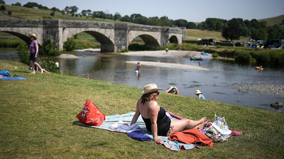People relax in the hot temperatures and cool off in the River Wharfe on July 19, 2022 in Burnsall, United Kingdom