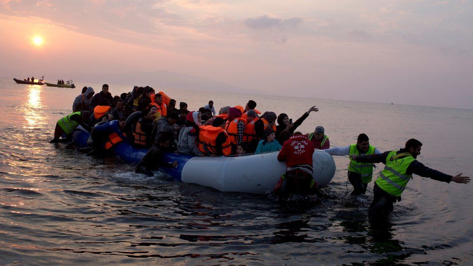 Volunteers help migrants and refugees on a dingy as they arrive at the shore of the north-eastern Greek island of Lesbos, after crossing the Aegean sea from Turkey on 20 March, 2016.