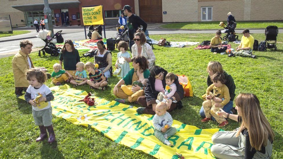 Women and children sitting on a banner outside the prison