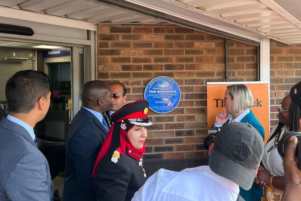 People look at a circular blue plaque commemorating the 75th anniversary of the first Windrush arrivals