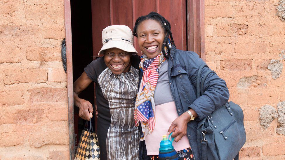A photo of Martha and a friend standing outside a home in Zimbabwe