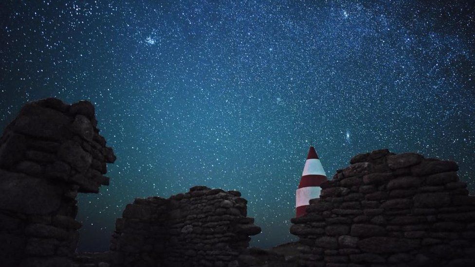Stars over rocky walls and a lighthouse