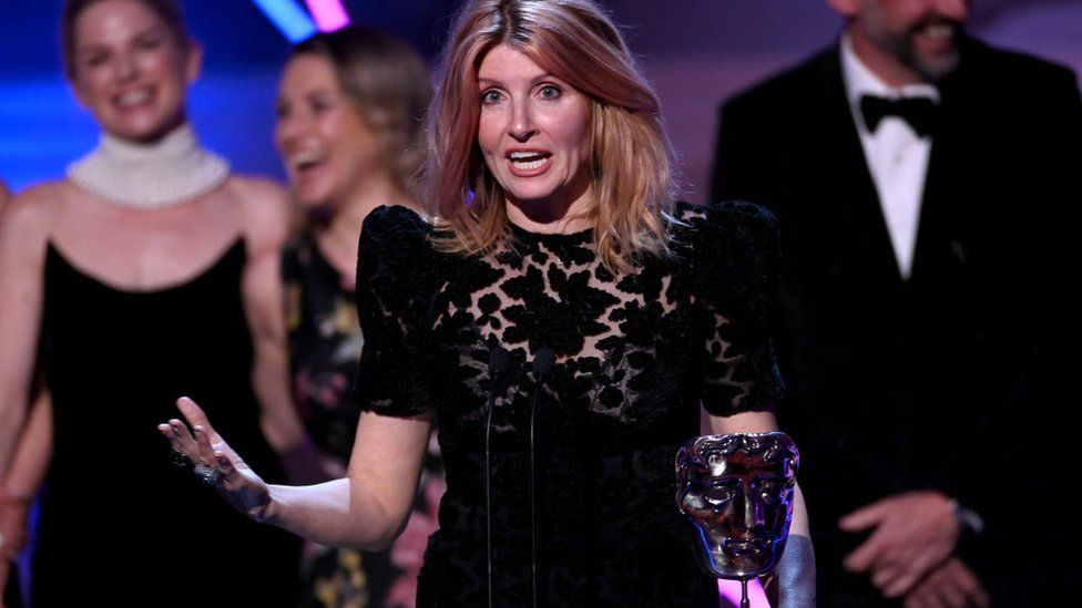 Bad Sisters actress Sharon Horgan accepts the award for Best Drama Series. She's in the middle of an acceptance speech and looks animated as she addresses the audience. She's wearing a black dress with a cutout pattern