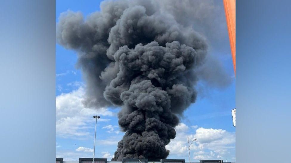 Thick black smoke in the blue sky, coming from an industrial unit