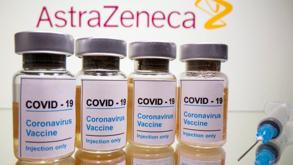 Флаконы с наклейкой «COVID-19 / вакцина против коронавируса / только для инъекций» и медицинский шприц перед логотипом AstraZeneca