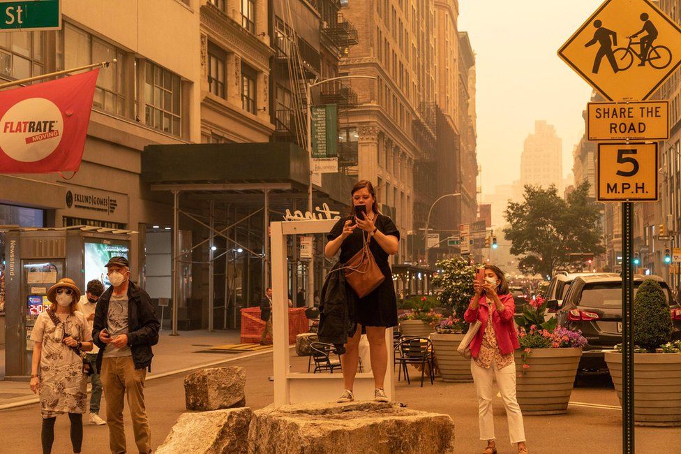People take photos and wear face masks on 7 June 2023 in New York, US, because of bad air quality brought in by smoke of Canadian wildfires