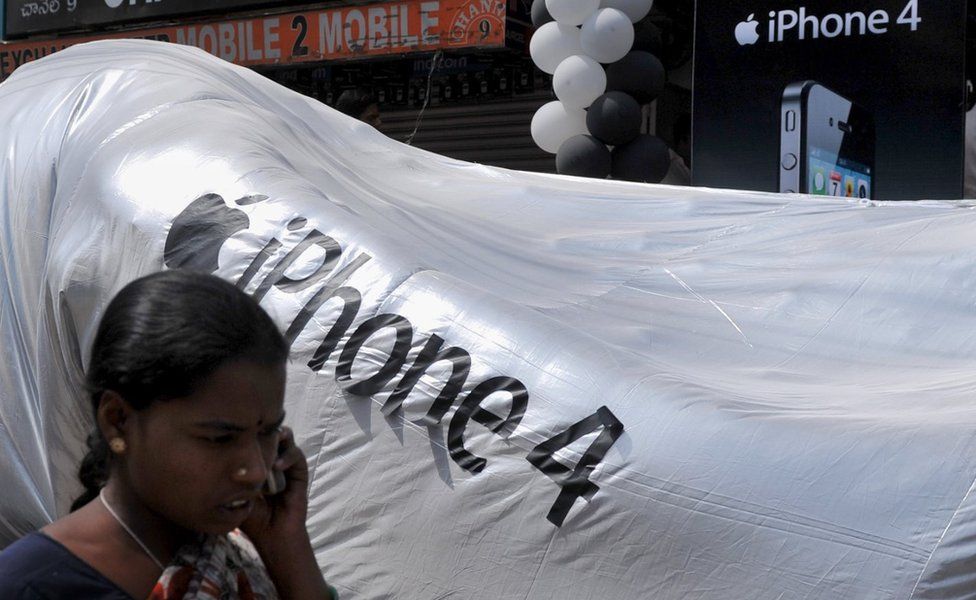 An Indian woman talks on her mobile phone as she walks past the logo of the iPhone 4 during its launch by provider Aircel in Hyderabad on May 27, 2011.