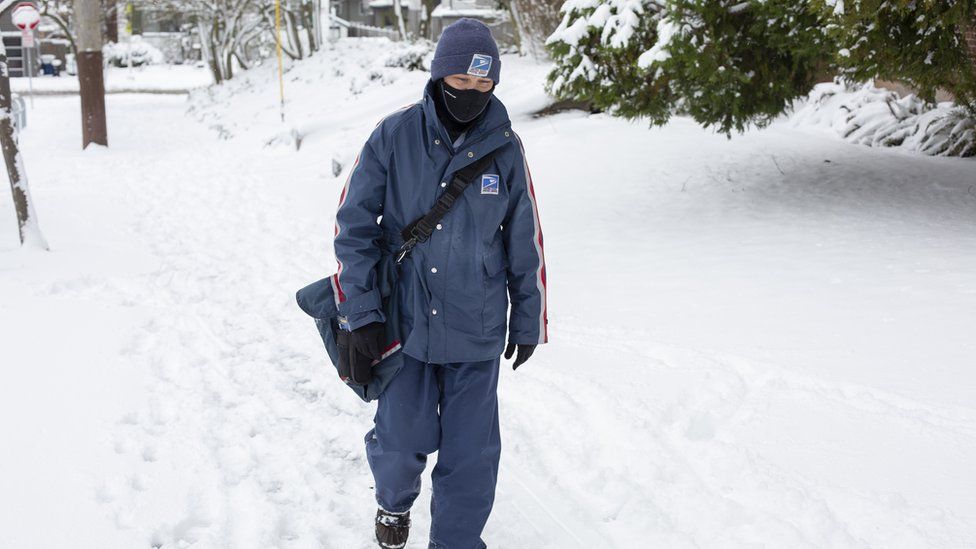 A postman, wrapped up, walks through snow in one community