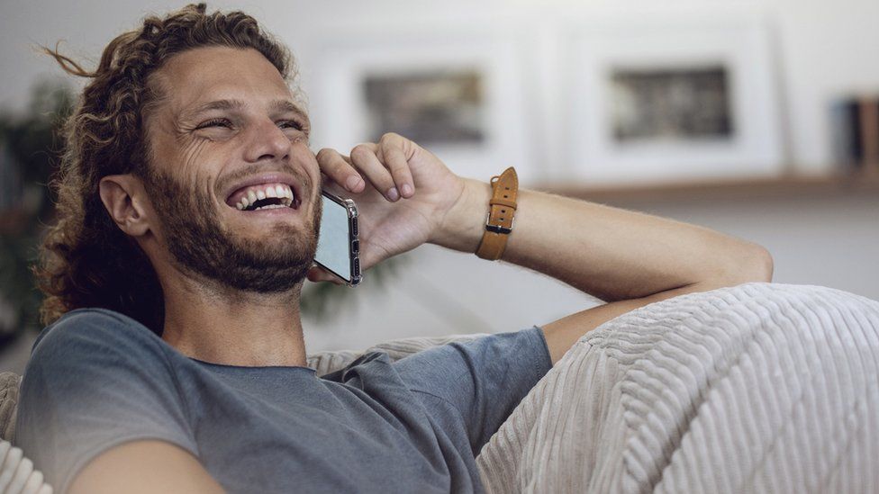 A man laughs while talking on the phone in this stock image
