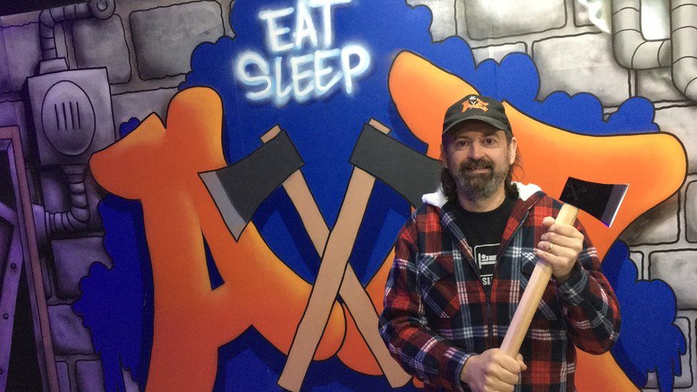 Pete George delante de un cartel de eat sleep axe sujetando un hacha