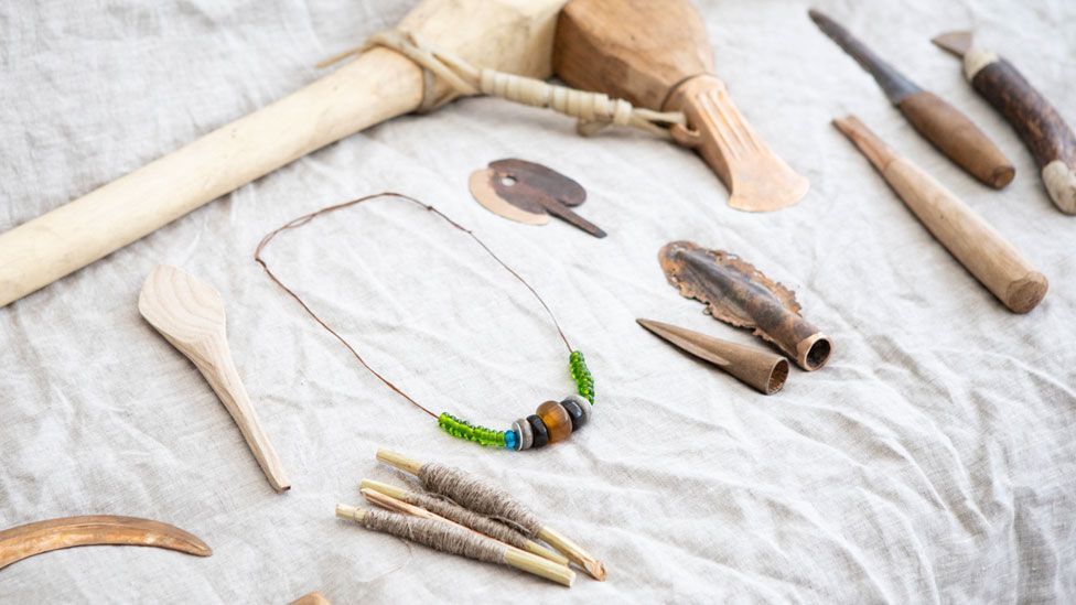 A range of replica and original Bronze Age items including a colourful necklace of glass beads and wooden handled tools