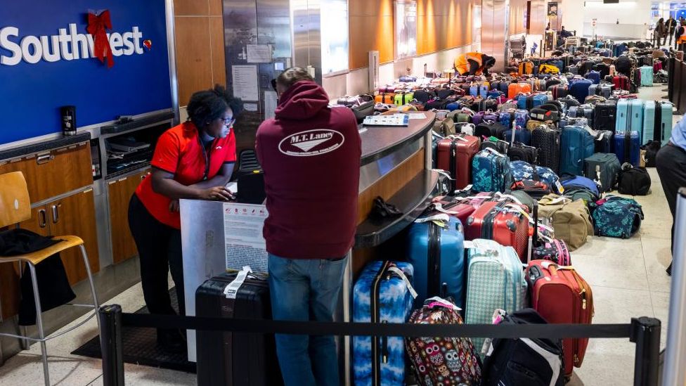 A passenger gets help from a Southwest agent amid a pile of suitcases