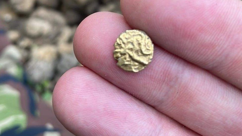 A hand holds a tiny gold coin