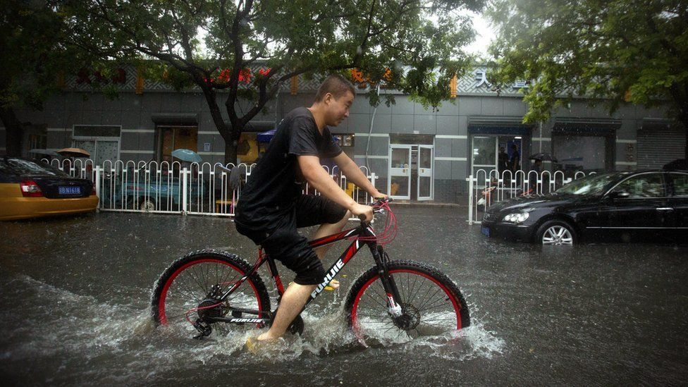 A bicyclist rides down a flooded side street in the rain in Beijing, Wednesday, July 20, 2016.