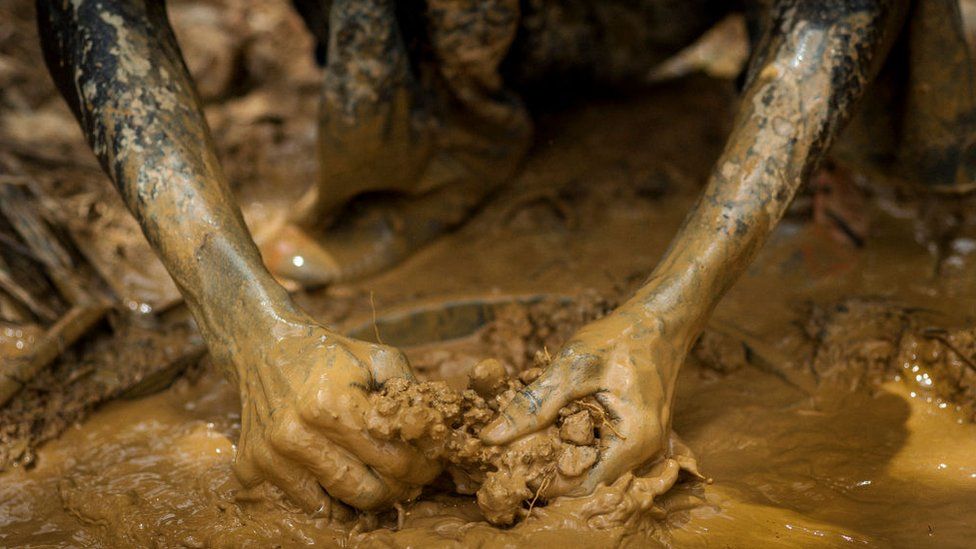 A Galamseyer, illegal gold panner, clears by hand mud and sand as he works on a gold field in Kibi on April 10, 2017