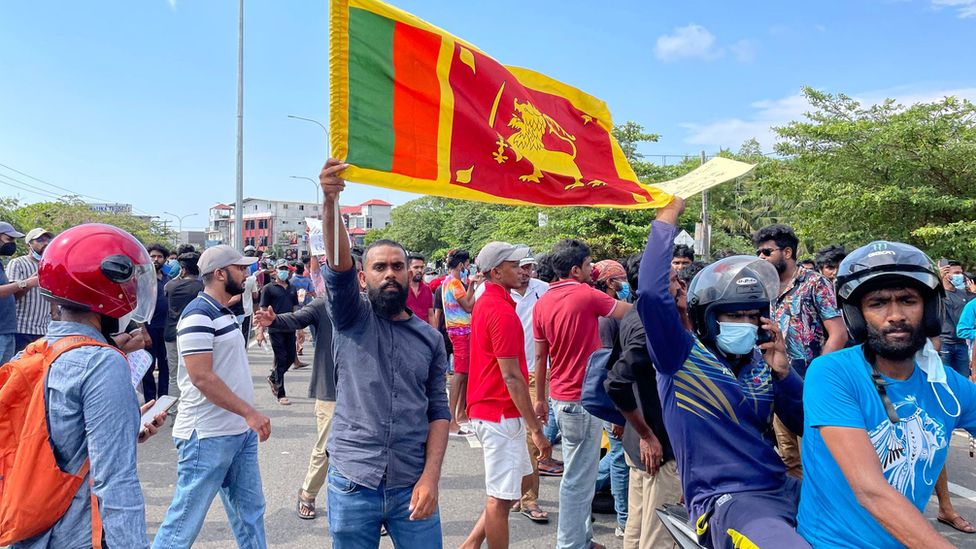Протестующий держит флаг Шри-Ланки среди толпы демонстрантов в Коломбо