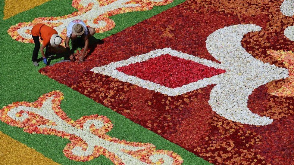 Two people work on the edge of a carpet design