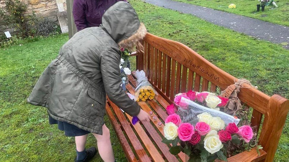 Ali and Rob Clark's daughter places flowers on a memorial bench outside St Mary's Church, Elloughton