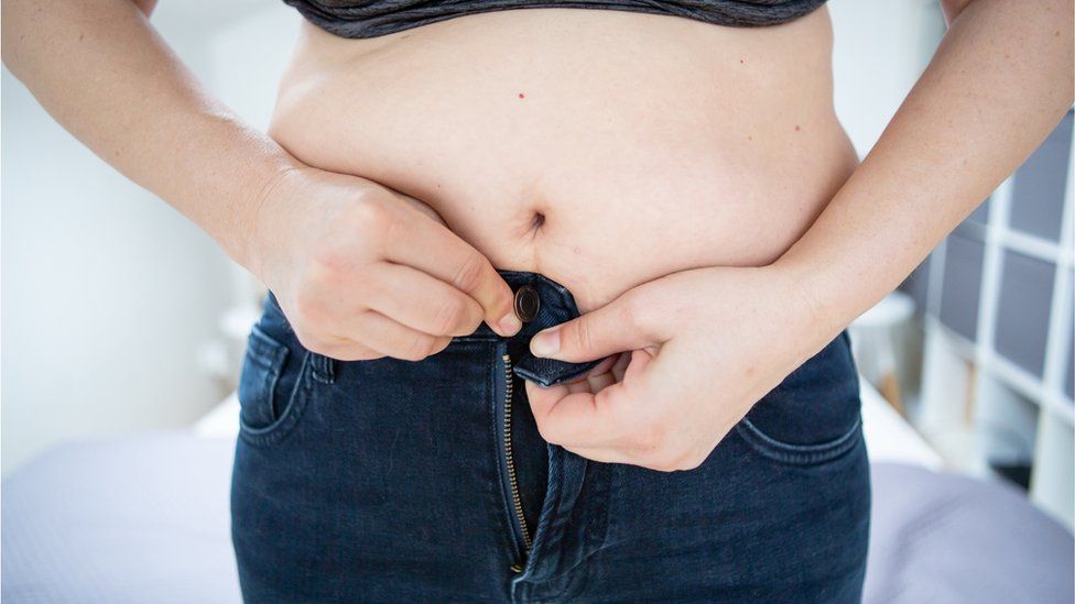 Overweight woman struggling to do her pants up - stock photo