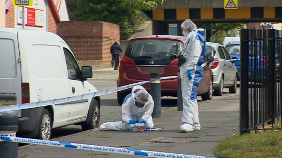 Two forensic officers examine an item on the pavement