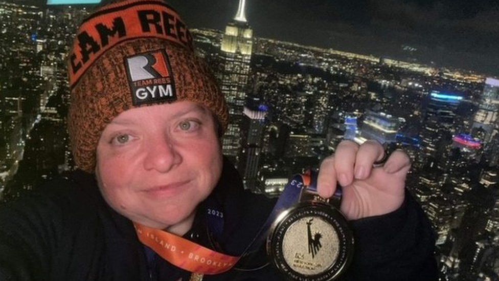 Kerrie Aldridge posing with medal with New York skyline in background