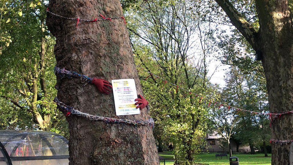 Trees on St Matthews Piece with a poster about the meeting and bunting with gloves hugging the tree.