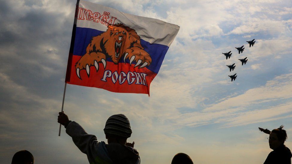 A Russian boy waves flag with slogan "Russia forward" as "The Russian Knights" an aerobatic demonstration team of the Russian Air Force perform during the Moscow International Aviation and Space Salon