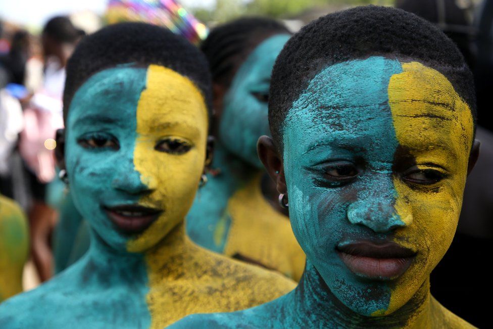 Two youths wear mirroring face paint in turquoise and yellow.