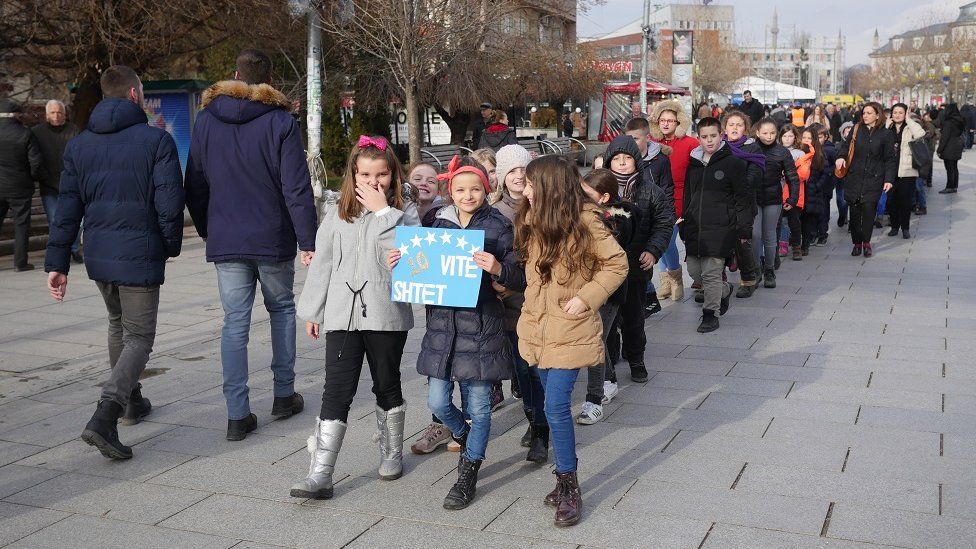 Young children walk through Pristina holding a signing celebrating Kosovo's 10th birthday.