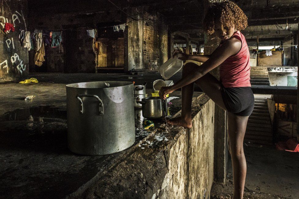 Girl washing the dishes in the main stairway of the occupied IBGE building, 'Favela' Mangueira community, Rio de Janeiro, Brazil.