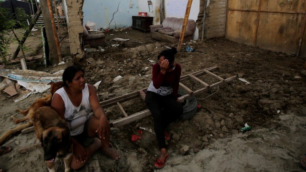 Women sit next to a flooded home damaged after heavy rain in Castilla district of Piura, northern Peru, March 16, 2017