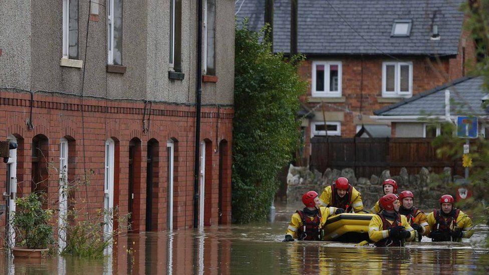 Firefighters pull a boat as they wade down a flooded street in St Asaph