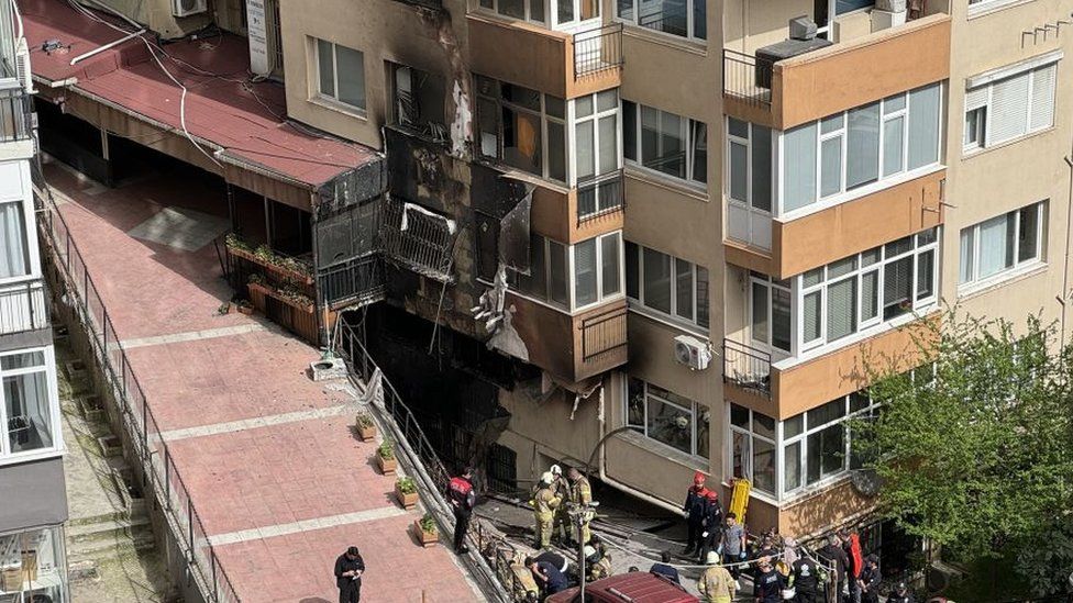 Firefighters crowd around a building that is charred at the base