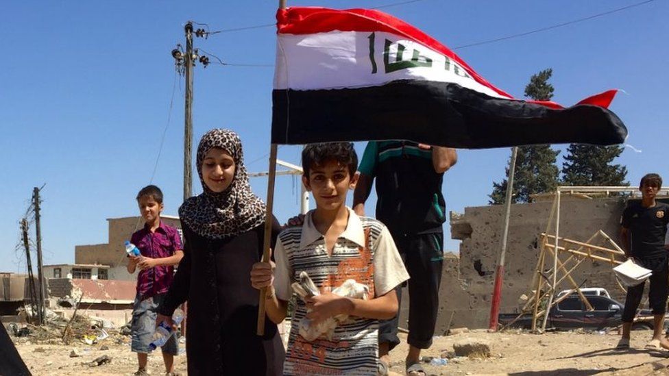 A young boy holds up a flag as he makes his way to safety