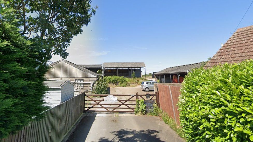 Wooden entrance gate to farm, with tree and bushes either side