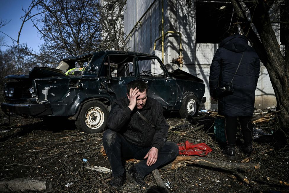 A man sits outside his destroyed building after bombings on the eastern Ukraine town of Chuhuiv on 24 February 2022