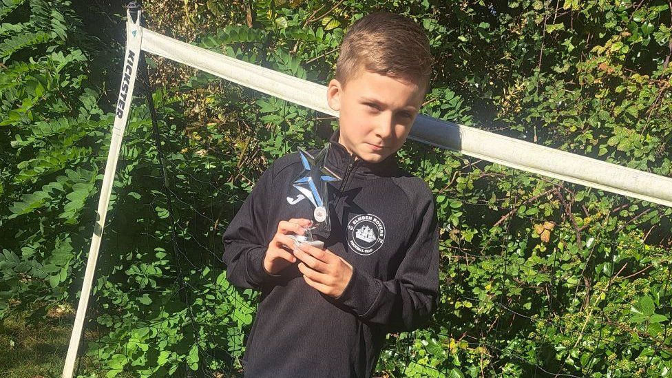 Harry standing in front of small football goals with a trophy.