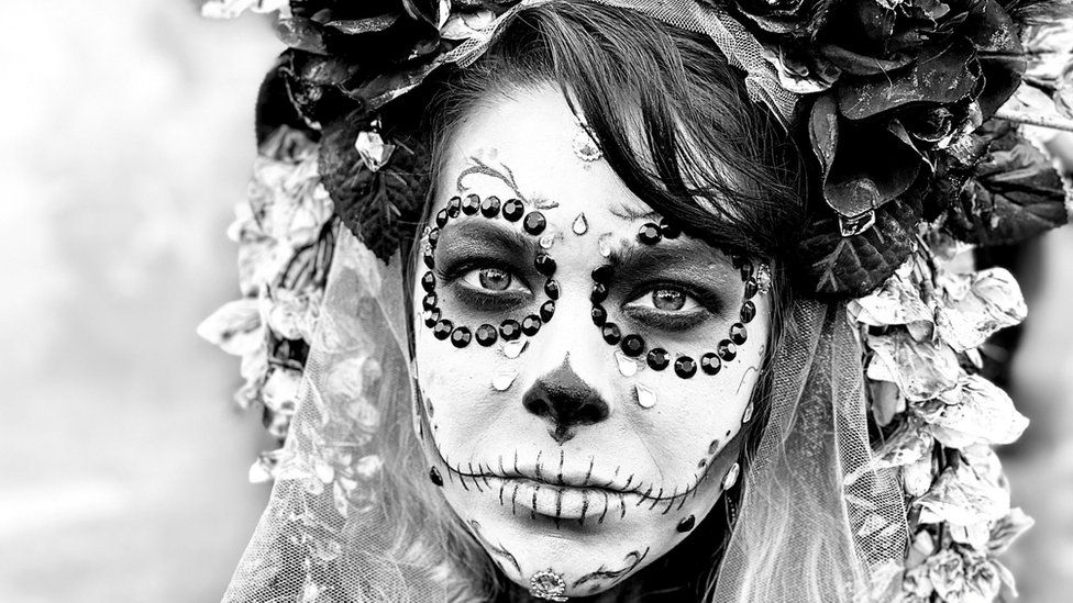 A photo of a woman dressed in a day of the dead costume, with white makeup and black eyes
