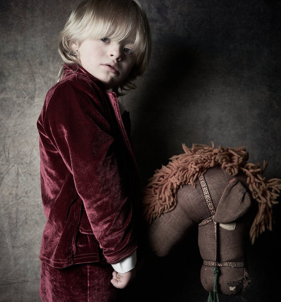 Austin, from Hexham, wearing a red velvet suit and holding a brown hobby horse