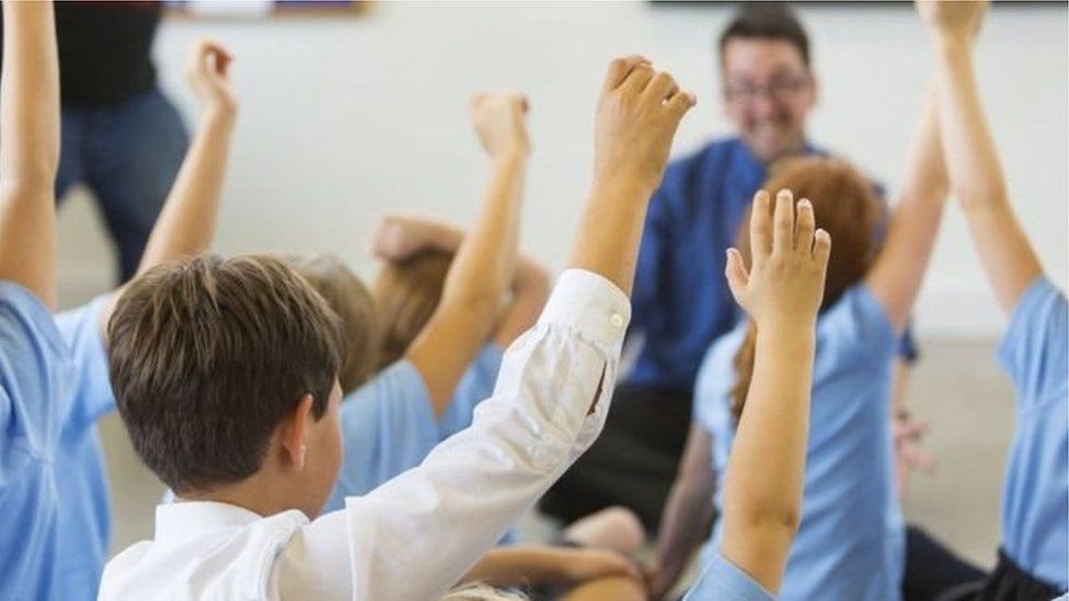 Children in a classroom with their hands raised