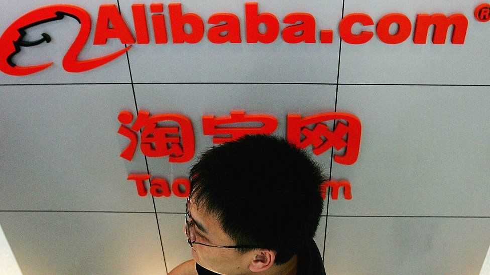 Man walks in front of an Alibaba logo