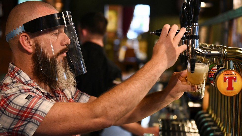 Man pours pint while wearing PPE visor