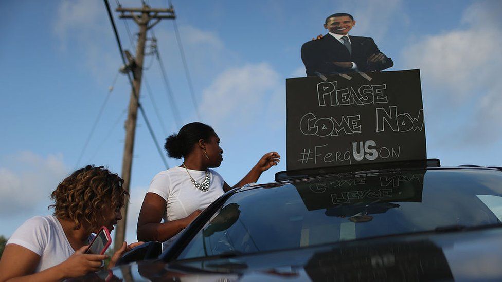 Demonstrators carry a sign with a picture of Barack Obama reading, "Please Come Now," on August 17, 2014 in Ferguson