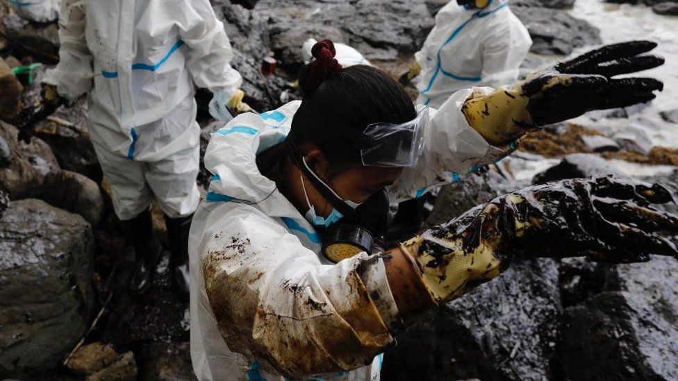 Men in protective suits collect oily waste on a beach