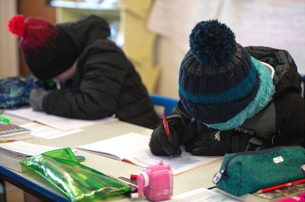 Children wear coats, hats and gloves in their classroom